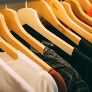 A close-up view of a row of clothes on wooden hangers, showcasing various fabrics and colors in a wardrobe setting.